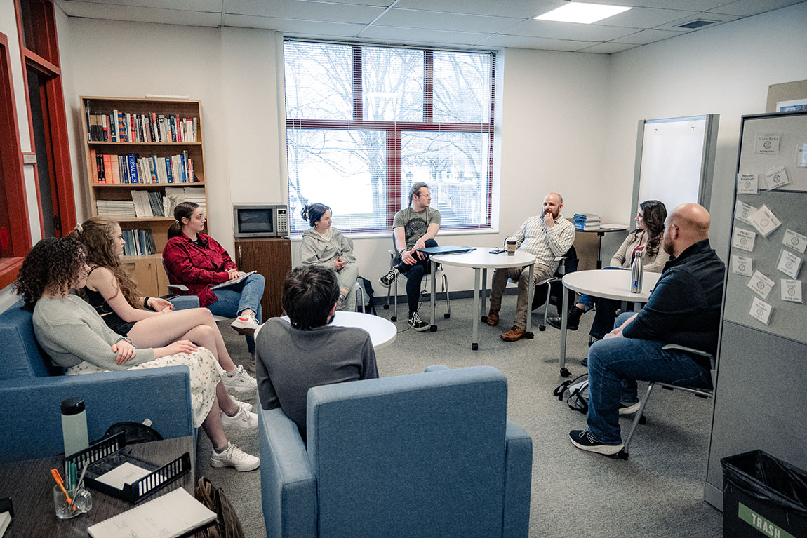 A group of college students and a college professor sit in a circle and have a discussion